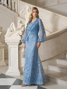 A woman wearing the Social Queen Hand-Beaded Lace Mermaid Dress stands indoors by a grand staircase, holding a small bag, with marble statues and ornate railings in the background.