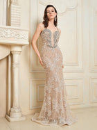 A woman models the Social Queen Hand-Beaded Sequin Embroidered Cocktail Gown, a fitted, floor-length nude dress with silver sequin details, paired with elegant lace trim, set against an ornate cream wall and fireplace.