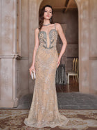 A woman stands indoors wearing the Social Queen Hand-Beaded Sequin Embroidered Cocktail Gown, a floor-length, sleeveless beige dress with silver details, while holding a small clutch.