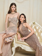 Two women showcase Social Queen’s Hand-Beaded Sequin Halter Mermaid Gown in a lavish room—one standing in the fitted mermaid silhouette, the other seated on a cream and gold chair, both dressed in nude-toned eveningwear.