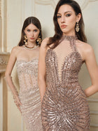 Two women pose indoors against a cream wall, each in fitted mermaid gowns with statement jewelry. One wears the Social Queen Hand-Beaded Sequin Halter Mermaid Gown, dazzling in champagne sequins and a chic halter neckline.