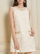 A woman wearing the Social Queen Hand-Beaded Silk Wool Embossed Dress, a cream tweed mini with an A-line cut, gold bead details, and front pockets, stands against a light-colored wall.