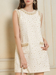 A woman wearing the Social Queen Hand-Beaded Silk Wool Embossed Dress, a cream tweed mini with an A-line cut, gold bead details, and front pockets, stands against a light-colored wall.