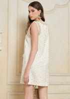 A woman in a Hand-Beaded Silk Wool Embossed Dress by Social Queen, sleeveless and cream-colored with pearl trim, stands facing backward and looks over her shoulder in an ornate interior.