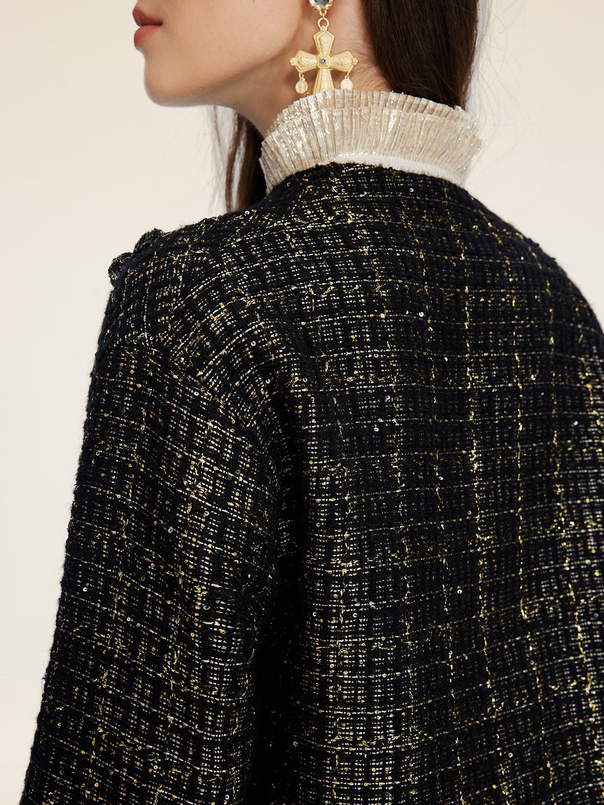 A person wearing the Social Queen Hand-Beaded Tweed Fringe Jacket, featuring black-and-gold tweed with a metallic collar and large star-shaped earrings, shown from the side.