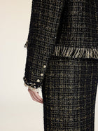 A person wearing the Social Queen Hand-Beaded Tweed Fringe Jacket, featuring black-and-gold tweed, decorative sleeve buttons, fringe accents, and a chic cropped fit.