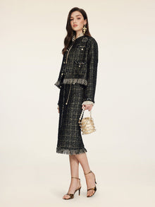 A woman wears the Social Queen Hand-Beaded Tweed Fringe Jacket, styled with a dark skirt suit, gold earrings, metallic heels, and a small gold handbag, standing against a plain light background.