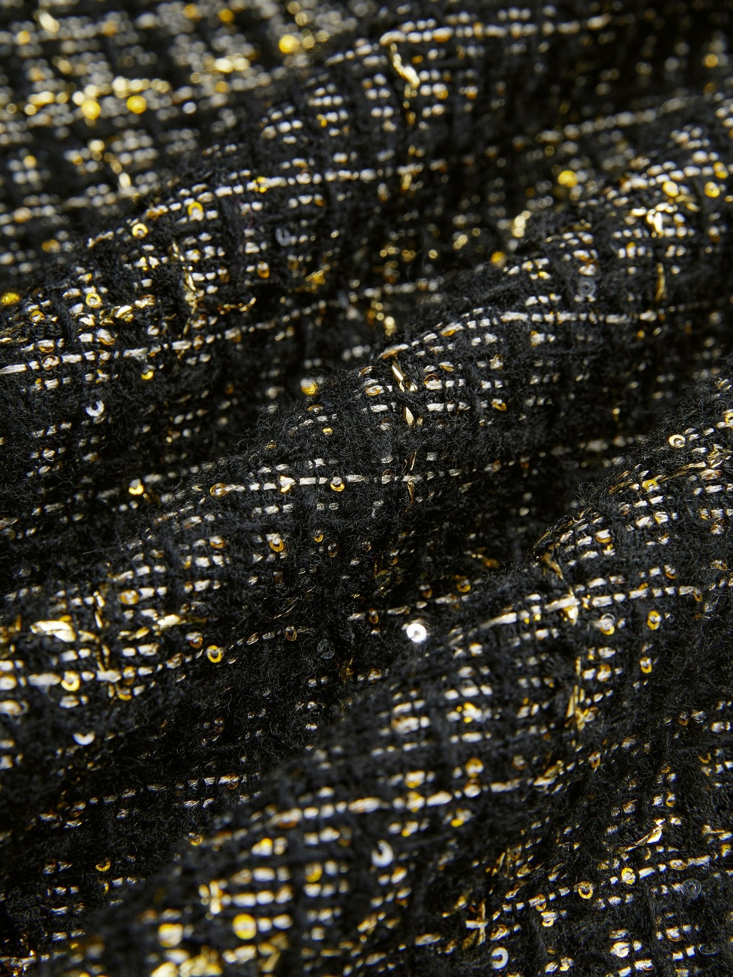 Close-up of hand-beaded detailing on Social Queen's Hand-Beaded Tweed Fringe Jacket, featuring gold and white threads and sequins forming a grid-like pattern on black-and-gold tweed.