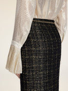 A person wearing a shimmery, pleated long-sleeve blouse and the Social Queen Hand-Beaded Tweed Fringe Slit Skirt, photographed from the waist down.