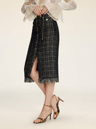 A person wears the Social Queen Hand-Beaded Tweed Fringe Slit Skirt with a light long-sleeve top and metallic high-heeled sandals while standing against a plain background.