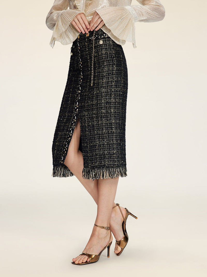 A person wears the Social Queen Hand-Beaded Tweed Fringe Slit Skirt with a light long-sleeve top and metallic high-heeled sandals while standing against a plain background.