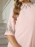 A woman wearing the Social Queen Hand-Embellished A-Line Dress with beaded collar and sleeves stands by a staircase.