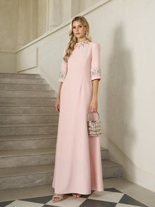 A woman stands on stone stairs holding a small handbag, wearing the Social Queen Hand-Embellished A-Line Dress in pale pink, floor-length with half sleeves.