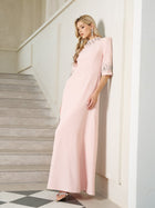 A woman wearing the Social Queen Hand-Embellished A-Line Dress in light pink stands indoors by a staircase, showcasing its floor-length silhouette and silver details.