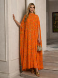A woman indoors wears the Social Queen Hand-Embellished Floral Caftan Dress with a cape design, paired with a beaded handbag and gold sandals—an ideal choice for chic resort style.