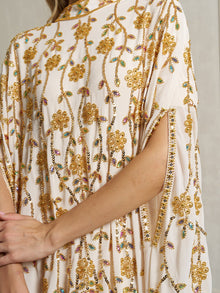 Close-up of a person wearing the Social Queen Hand-Embellished Floral Caftan Dress, a cream-colored chiffon piece featuring intricate gold embroidery, beading, and slit sleeves—perfect resort wear.