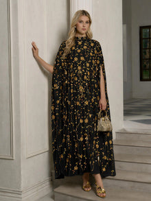 Indoors, a woman wears the Social Queen Hand-Embellished Floral Caftan Dress with gold patterns, paired with gold sandals and a small gold handbag.