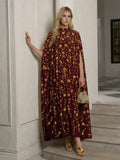 A woman stands in a room wearing the Social Queen Hand-Embellished Floral Caftan Dress, paired with gold sandals and holding a small gold handbag.