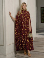 A woman stands in a room wearing the Social Queen Hand-Embellished Floral Caftan Dress, paired with gold sandals and holding a small gold handbag.