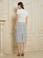 A woman stands indoors facing a wall, wearing a short-sleeve white top, gold high-heeled sandals, and the Social Queen Hand-Embellished Sequin Fringe Skirt.