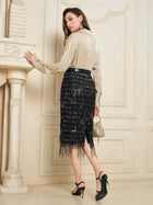 A woman stands indoors facing sideways, wearing a beige blouse, black heels, holding a small handbag, and styled in the Social Queen Hand-Embellished Sequin Fringe Skirt.