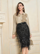 Indoors, a woman wears a beige blouse with floral embroidery and the Social Queen Hand-Embellished Sequin Fringe Skirt, holding a small gold handbag.