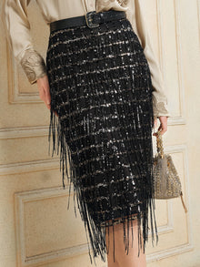 A person is wearing the Social Queen Hand-Embellished Sequin Fringe Skirt with a beige blouse, black belt, and holding a small gold handbag, standing against a cream-colored paneled wall.