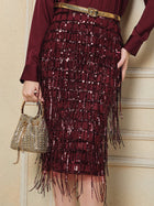 A person wears the Social Queen Hand-Embellished Sequin Fringe Skirt with a gold belt and holds a small, gold beaded handbag against a cream-colored wall.