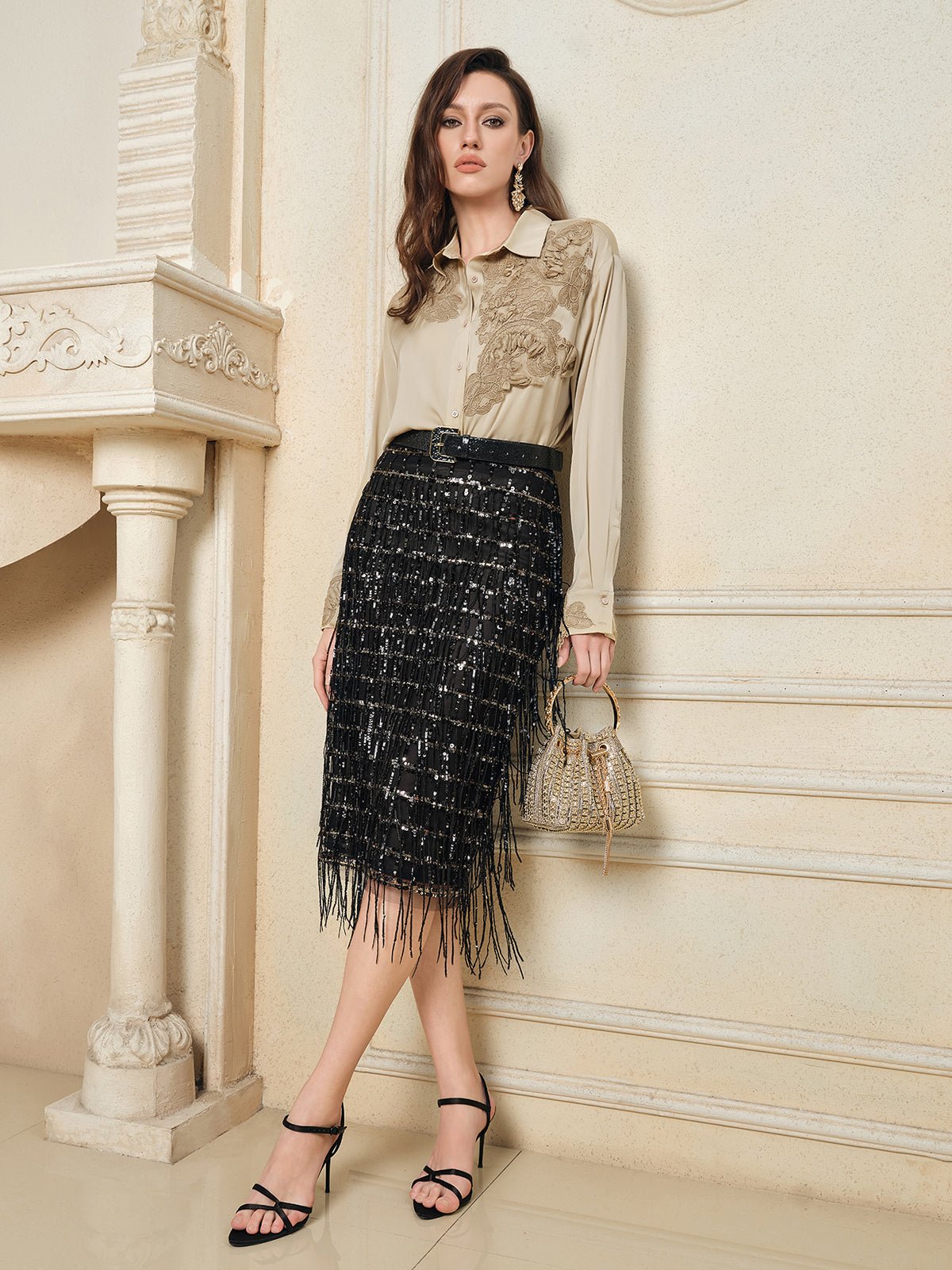 A woman stands indoors in a beige lace-detail blouse, the Social Queen Hand-Embellished Sequin Fringe Skirt, black heels, and holding a small handbag.
