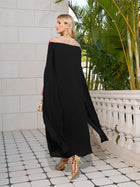 A woman in the Social Queen Hand-Embroidered Floral Cape Gown and gold heels stands on a tiled terrace, facing away, with greenery and a white balustrade behind her.