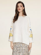 A woman models the Social Queen Hand-Embroidered Floral Jacquard Pullover with floral sleeve motifs, paired with a silver fringed skirt, against a plain background.