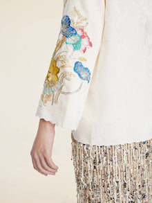 A person wearing the Social Queen Hand-Embroidered Floral Jacquard Pullover with floral sleeve embroidery, paired with a skirt featuring metallic fringe, sequins, and beaded embellishments.