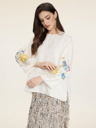 A woman models the Social Queen Hand-Embroidered Floral Jacquard Pullover, featuring intricate floral motifs, paired with a silver fringed skirt against a light background.
