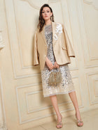 Indoors, a woman wears the Social Queen Hand-Embroidered Floral Silk-Wool Jacket over a silver sequin dress, paired with a decorative handbag and heeled sandals.