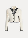 The Social Queen Hand-Embroidered Silk-Wool Cropped Tweed Jacket features a vintage-inspired white design with black buttons, black trim, and intricate embroidered black lace floral accents on the collar and upper chest.