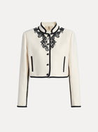 The Social Queen Hand-Embroidered Silk-Wool Cropped Tweed Jacket features a vintage-inspired white design with black buttons, black trim, and intricate embroidered black lace floral accents on the collar and upper chest.