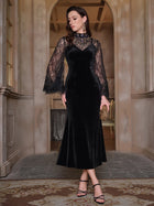 A woman stands indoors wearing the Social Queen Hand-Sewn Crystal Velvet Feather Mermaid Gown with sheer lace-detailed sleeves, an embellished neckline, black sandals, and a small clutch.