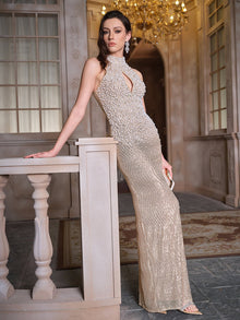 A woman poses by a stone railing in a chandelier-lit interior, wearing the Social Queen Hand-Sewn Pearl & Sequin Halter Gown.