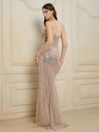 A woman in the Social Queen Hand-Sewn Radiant Crystal Mesh Pleated Gown, fitted and floor-length, stands before a decorative cream wall, glancing over her shoulder.