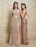 Two women pose indoors in Social Queen Hand-Sewn Radiant Crystal Mesh Pleated Gowns, featuring metallic patterns and high slits, standing against a beige decorative wall.