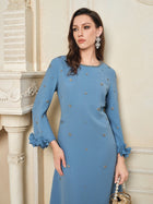 A woman in the Social Queen Handcrafted Beaded Floral A-Line Dress stands indoors near a fireplace, holding a round beaded purse and wearing large floral earrings.