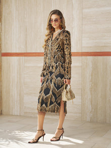 Woman in a black dress with gold details, gold earrings, sunglasses, and heels stands indoors holding a small gold handbag topped with the Social Queen Handcrafted Beaded Fringe Jacket.