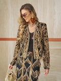 A woman stands against a beige wall, wearing the Social Queen Handcrafted Beaded Fringe Jacket with sunglasses, large earrings, and holding a small decorative handbag.