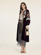 A woman radiates vintage glamour in the Social Queen Handcrafted Embroidered Velvet Jacket over a white blouse and sparkly fringed skirt, holding a metallic handbag and wearing heels against a plain backdrop.