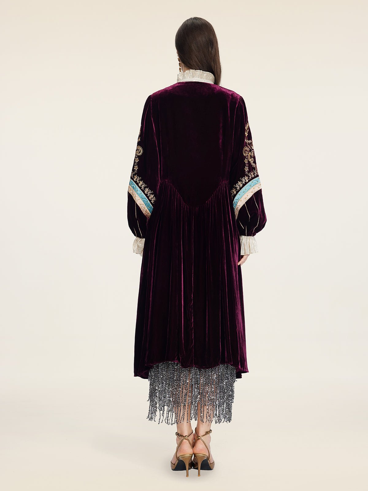 A person faces away, wearing Social Queen’s Handcrafted Embroidered Velvet Jacket with hand-applied pearls, paired with a silver fringe skirt and heels, for a look that channels vintage glamour.