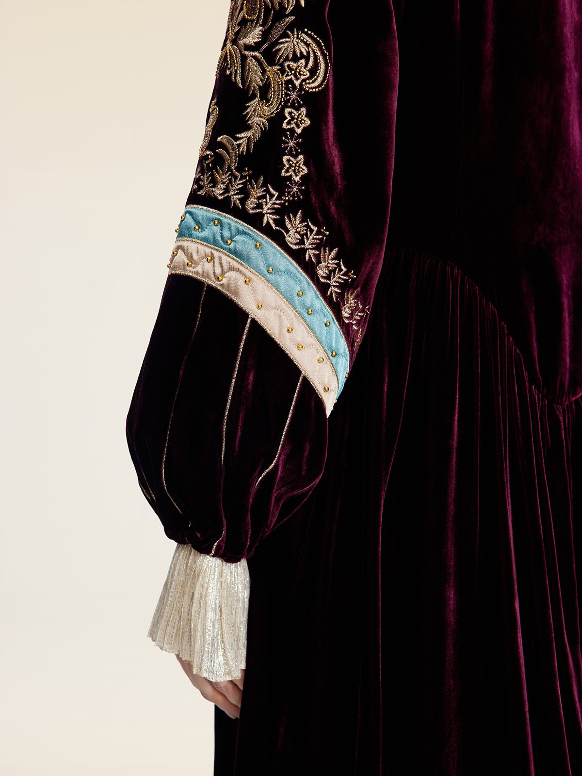 A close-up of a person wearing the Social Queen Handcrafted Embroidered Velvet Jacket, showcasing vintage glamour with ornate gold thread embroidery, blue accents, and hand-applied pearls on the sleeve.