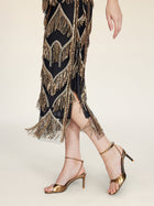 Wearing the Social Queen Handcrafted Fringe Sequin Halter Gown, this person stands elegantly in gold high-heeled sandals against a light background.