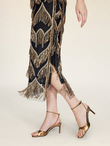 Wearing the Social Queen Handcrafted Fringe Sequin Halter Gown, this person stands elegantly in gold high-heeled sandals against a light background.