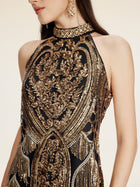 A woman wears the Social Queen Handcrafted Fringe Sequin Halter Gown, a sleeveless black and gold gown with intricate embroidery, sequins, and beaded details, paired with gold earrings.