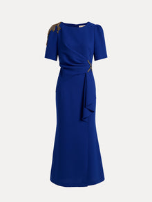 The Handcrafted Gold-Trimmed Slit Dress by Social Queen features gold accents on one shoulder and waist, short sleeves, and a draped fishtail silhouette in sapphire blue.